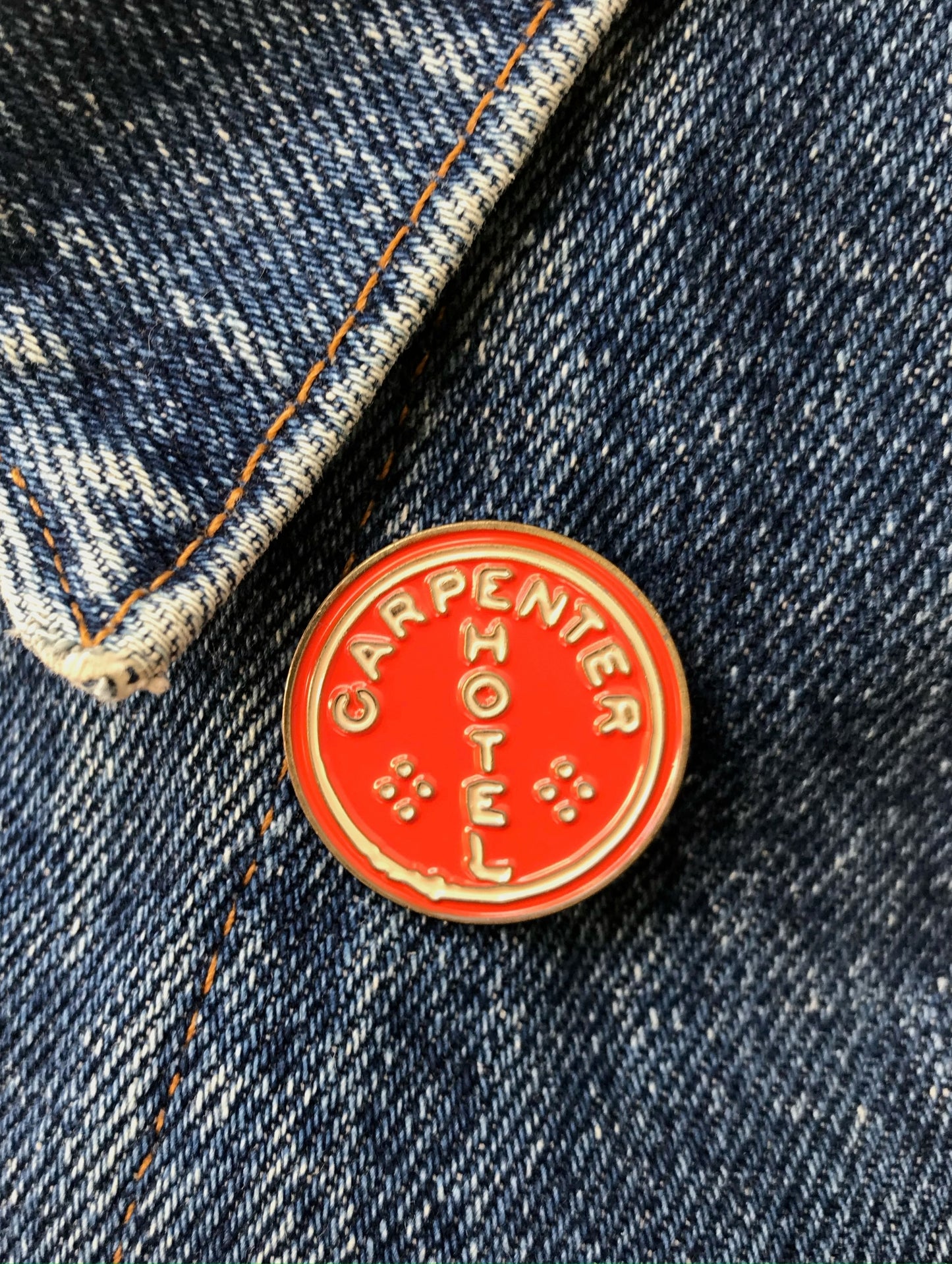 Red 'Carpenter Hotel' pin on a denim jacket background