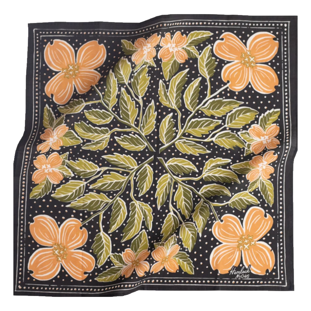 A multicolored bandana with a floral pattern, predominantly in black orange and green, laid out.